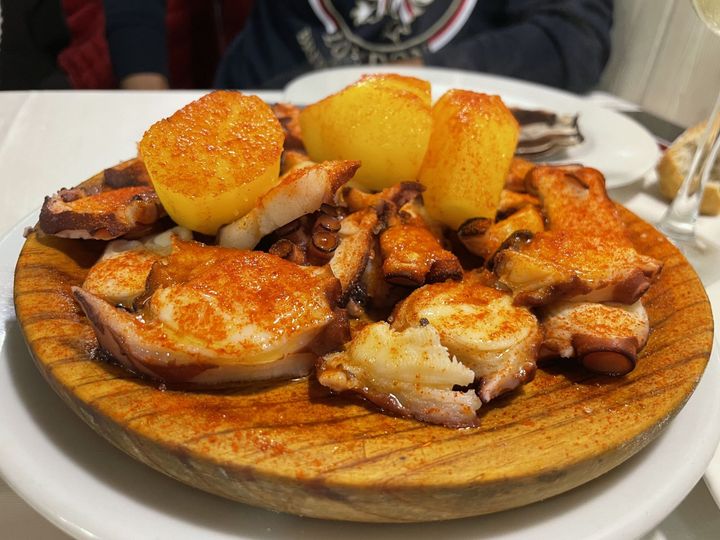 Mariscos mixtos a la parrilla y patatas en un plato de madera, servidos en una mesa.