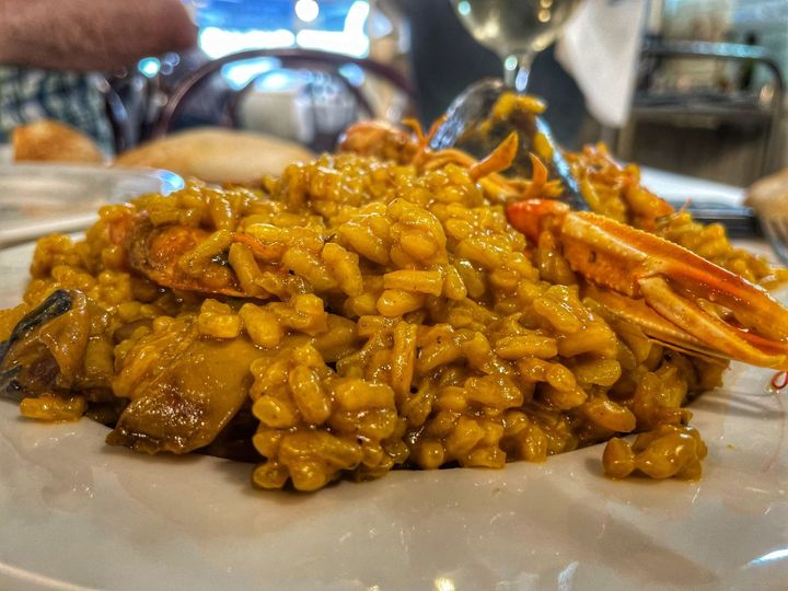 Gambas y risotto en un plato blanco en un restaurante, con la vajilla borrosa al fondo.
