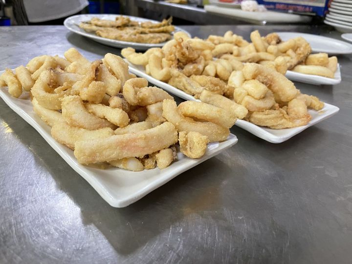 Platos de mariscos fritos dorados sobre una encimera de acero inoxidable en una zona de preparación de la cocina.
