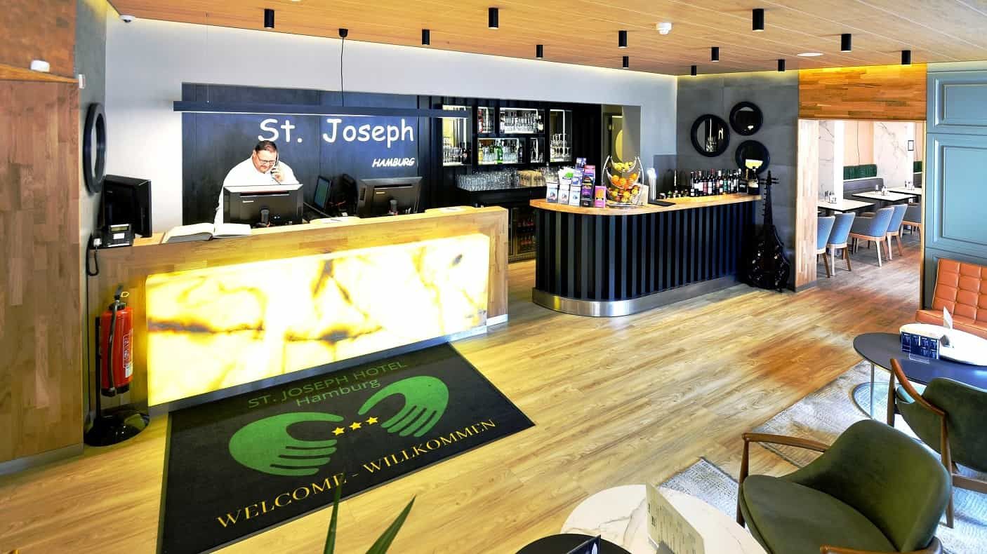 Hotelrezeption mit einem Mann am Tresen, Akzente aus Holz und Schwarz, helle Beleuchtung.