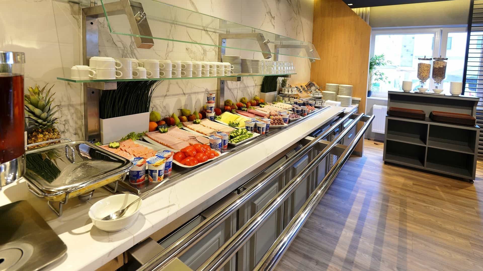 Frühstücksbuffet mit verschiedenen Speisen: Obst, Fleisch, Joghurt und Müsli.