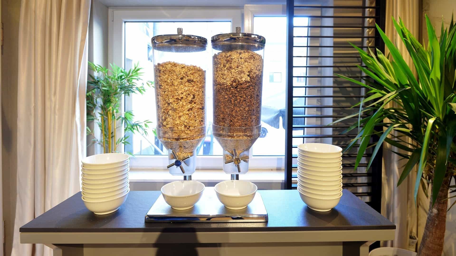 Müslispender mit Müsli, Schüsseln und eine Pflanze in der Nähe eines Fensters.