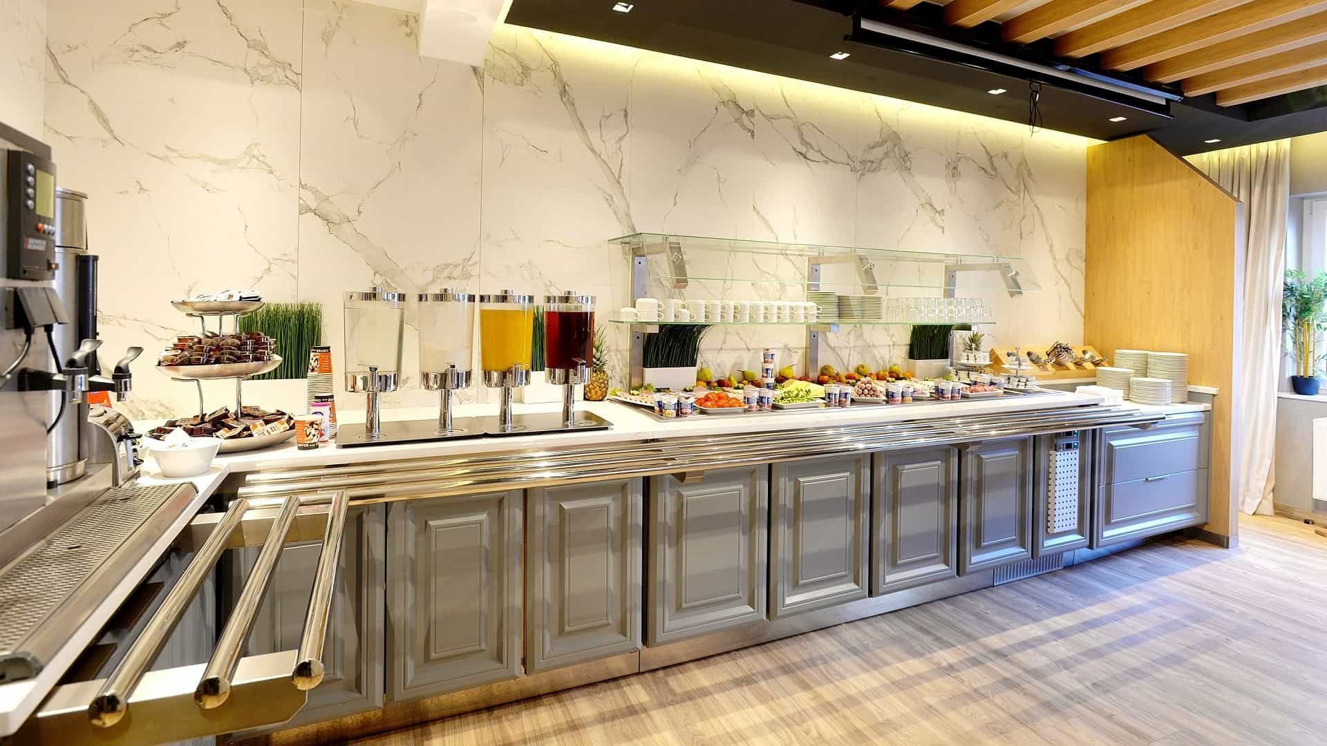 Frühstücksbuffet mit Saftspendern, Speisen und Servierbereich vor einer Marmorwand.