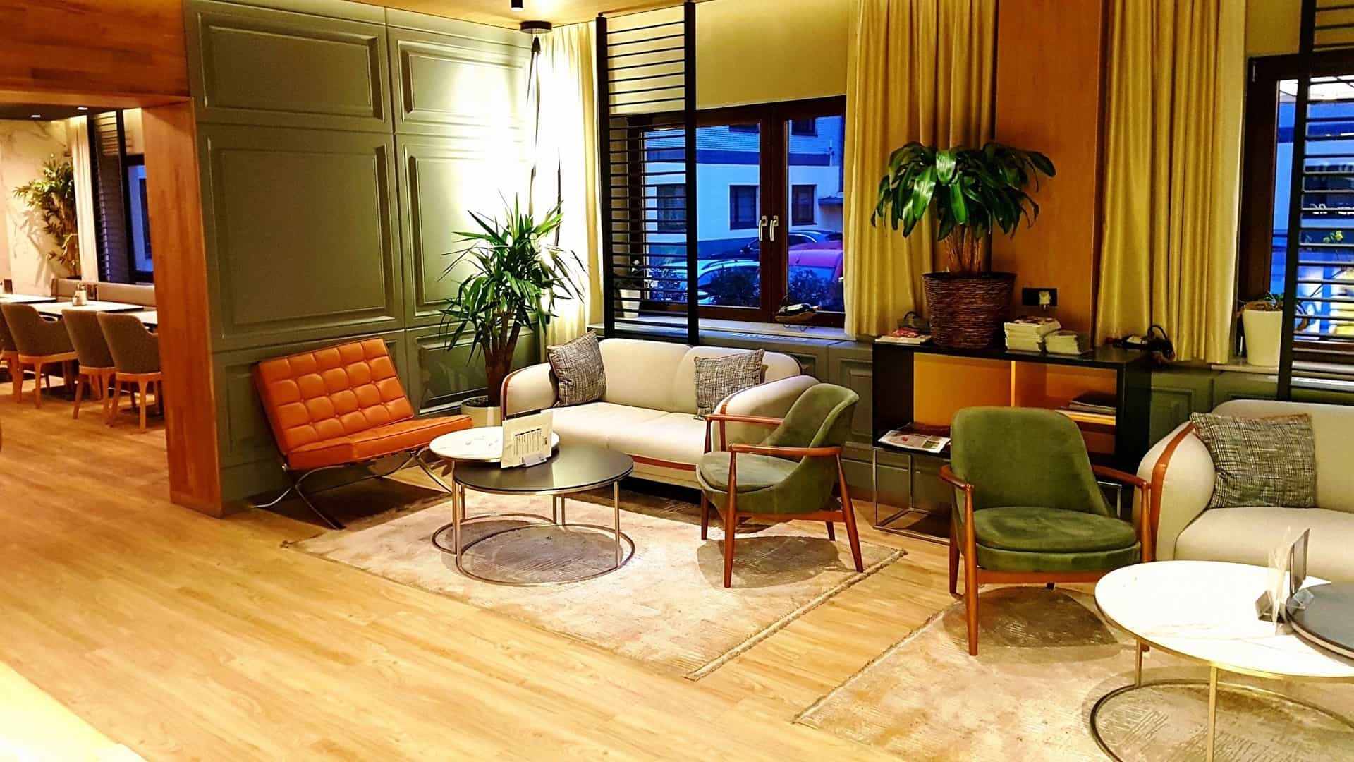 Ein moderner Loungebereich mit Sofa, Sesseln, Pflanzen und einem Fenster mit Blick auf die Stadt.