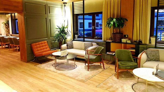 Ein moderner Loungebereich mit Sofa, Sesseln, Pflanzen und einem Fenster mit Blick auf die Stadt.