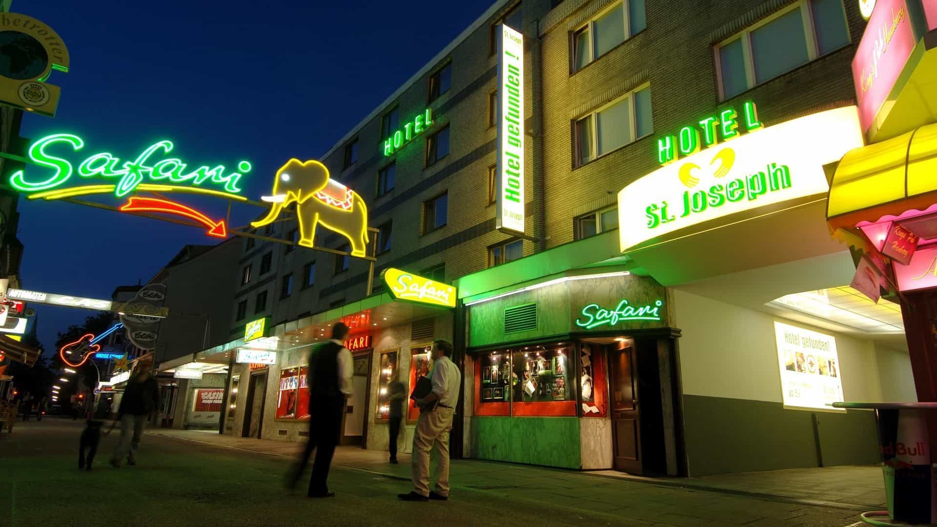Neonbeleuchtetes „Safari“-Hotelschild mit Elefantensilhouette, Menschen auf der Straße bei Nacht.