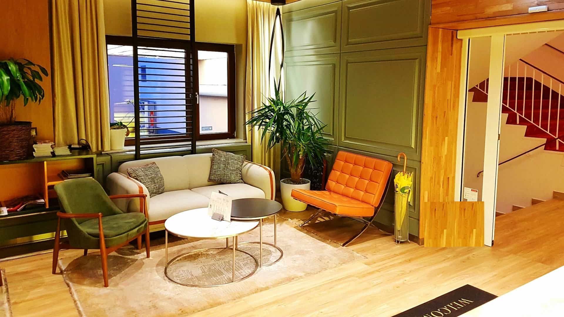 Wohnzimmer mit Sofa, zwei Sesseln, Couchtisch, Teppich, Fenster und Treppe.