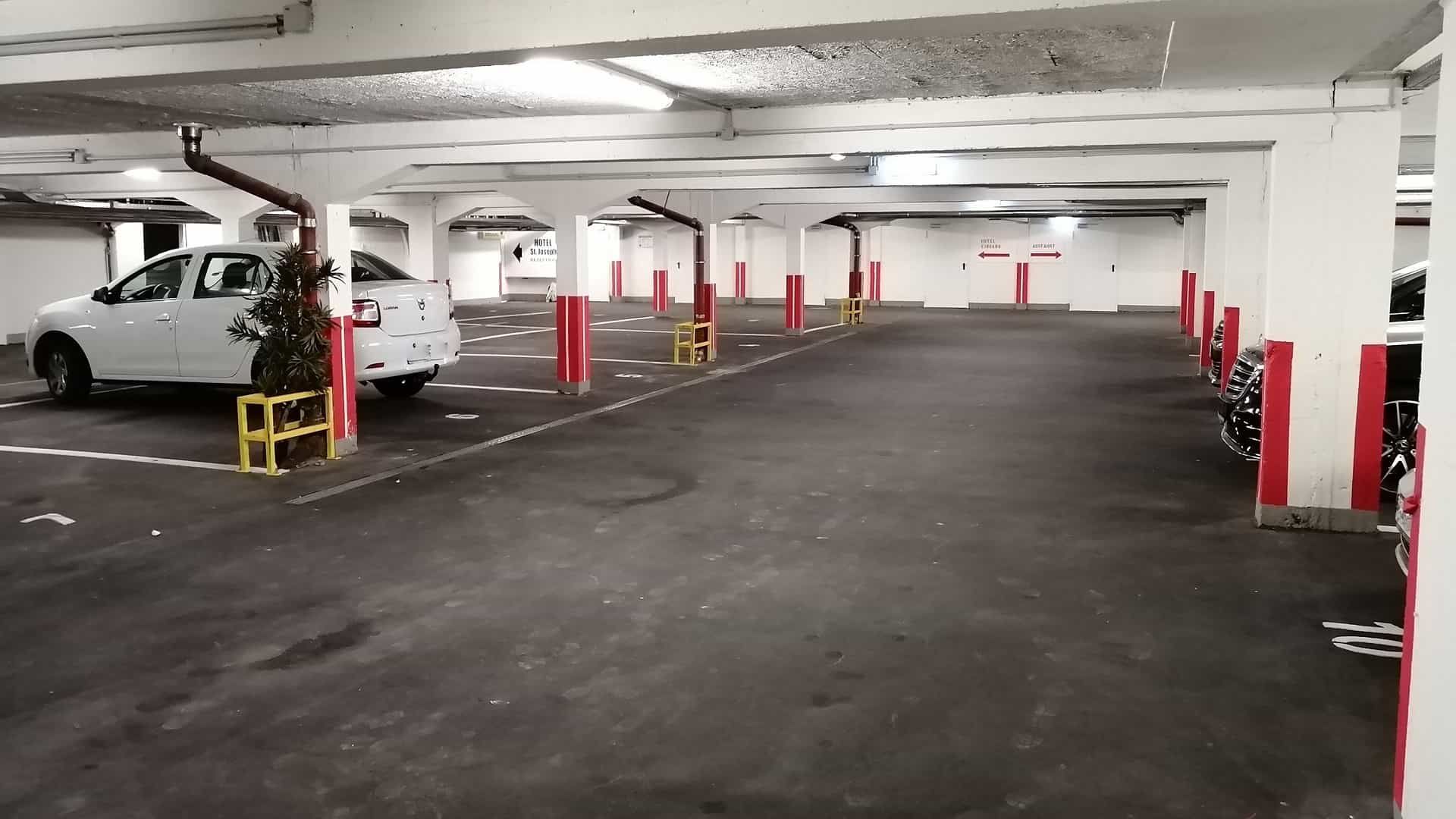 Leere Tiefgarage mit weißen Säulen und roten Akzenten. Ein weißer Pickup-Truck ist geparkt.