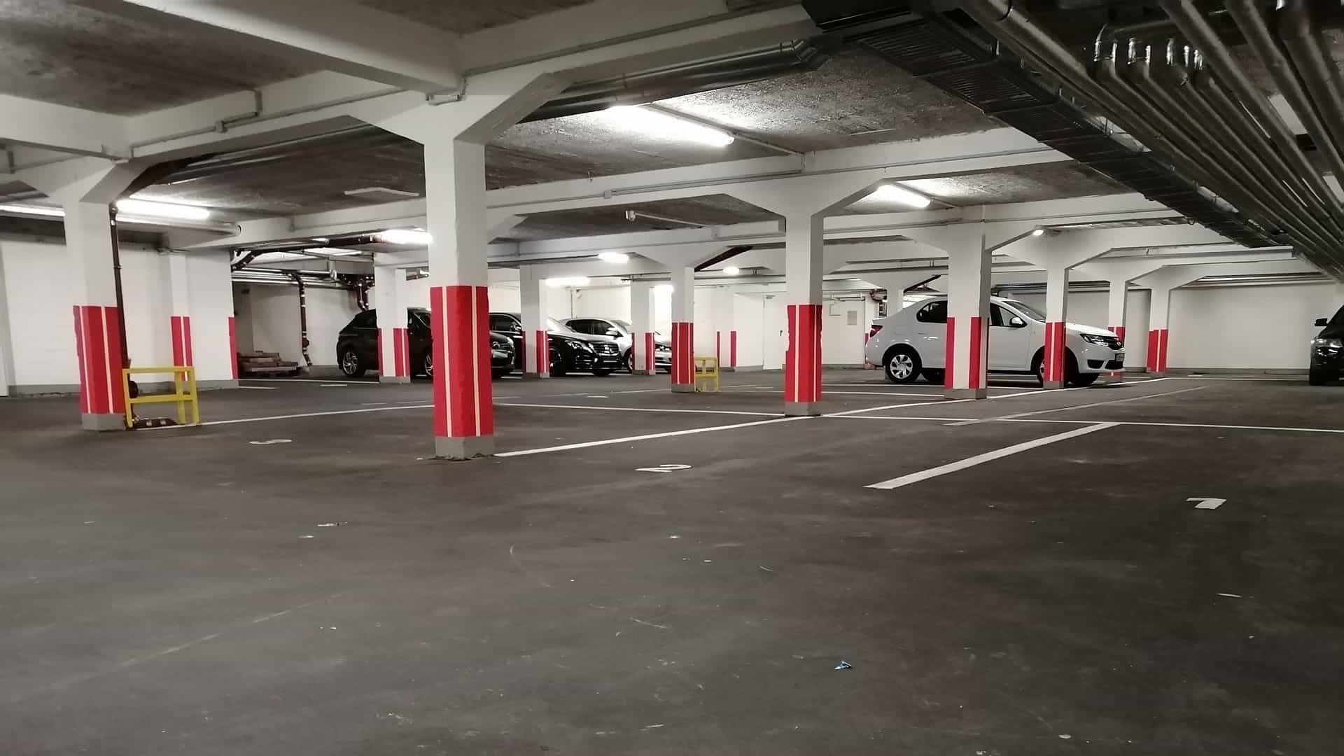 Parkhaus mit geparkten Autos, weißen Säulen und rot umwickelten Stützen.