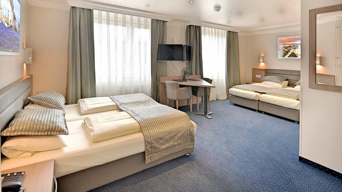 Hotelzimmer mit zwei Betten, Schreibtisch, Fernseher und blauem Teppich.