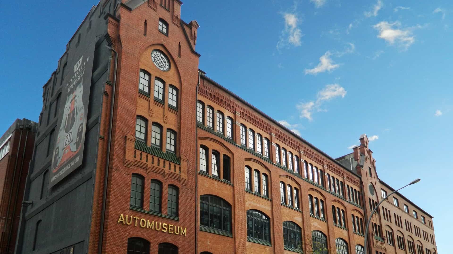 Backsteingebäude mit dem Schild „Automuseum“, blauem Himmel und einer großen Werbetafel.