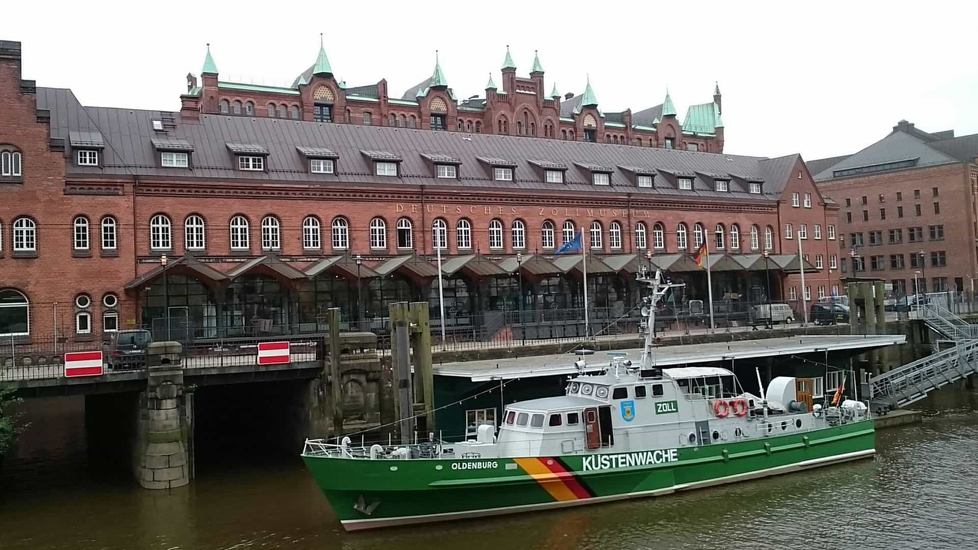 Ein grün-weißes Boot mit der Aufschrift „Küstenwache“ vor einem Backsteingebäude.
