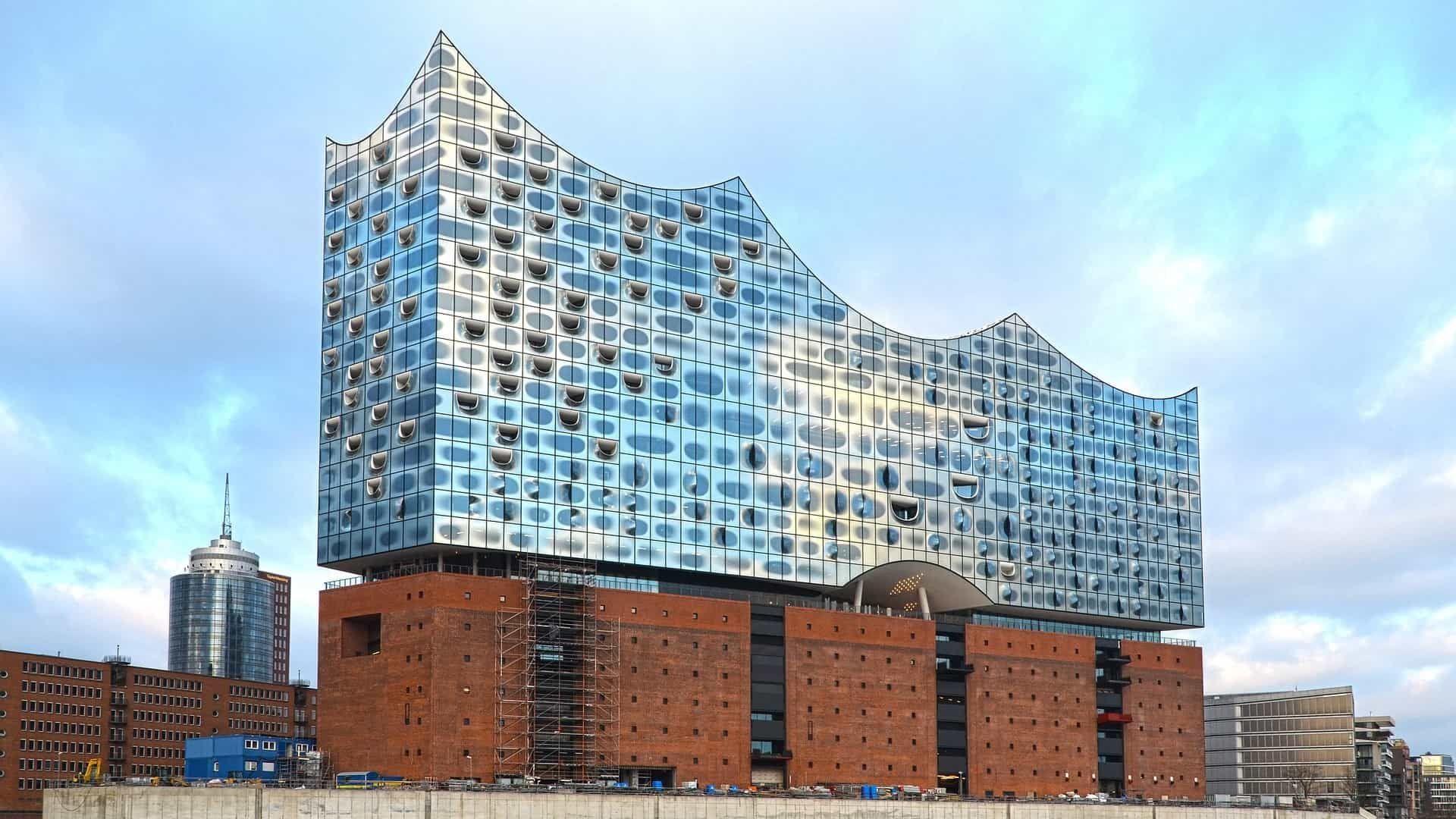 Die Elbphilharmonie in Hamburg, Deutschland. Blaue Glasfassade auf einem Backsteinsockel vor bewölktem Himmel.