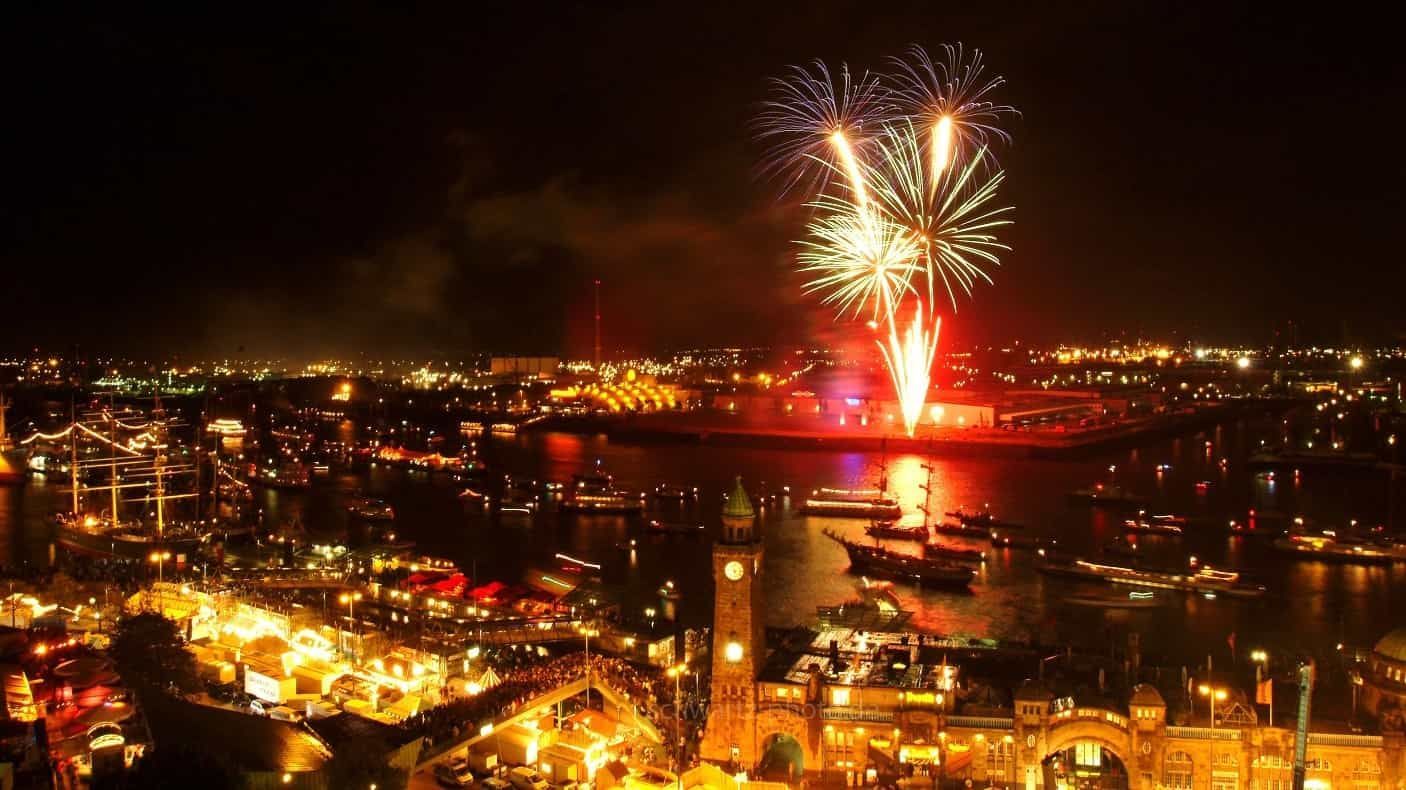 Nachts explodieren Feuerwerkskörper über der Stadt und spiegeln sich im Wasser darunter.