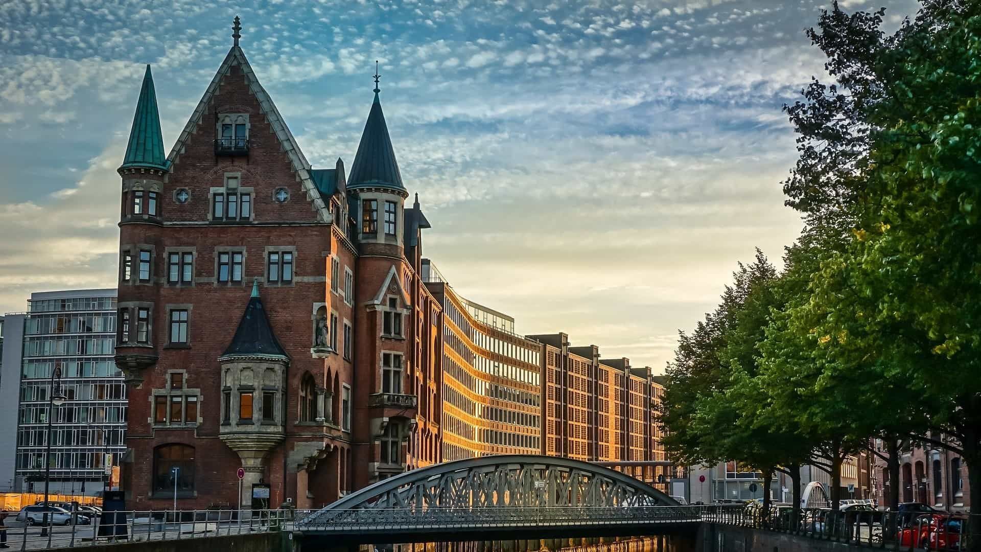 Backsteingebäude mit Türmchen, Brücke über einen Kanal in Hamburg, Deutschland, mit Bäumen und modernen Gebäuden.