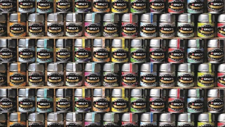 Reihen kleiner Gläser mit bunten Etiketten auf einem Regal, vermutlich eine Ladenauslage.