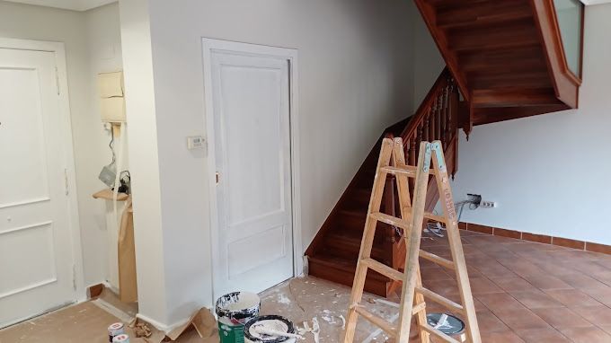 Una escalera de madera, dos puertas blancas y una escalera de mano en una habitación con paredes claras.