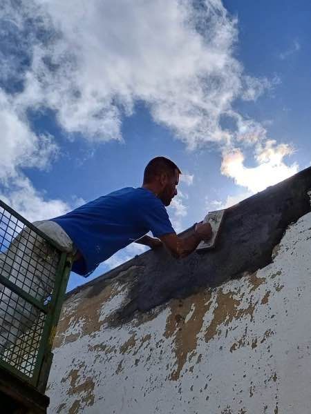 Un hombre con una camisa azul está enyesando una pared.