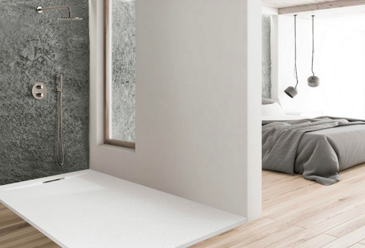Baño minimalista con lavabo blanco, pared de piedra y puerta abierta a un dormitorio con cama.