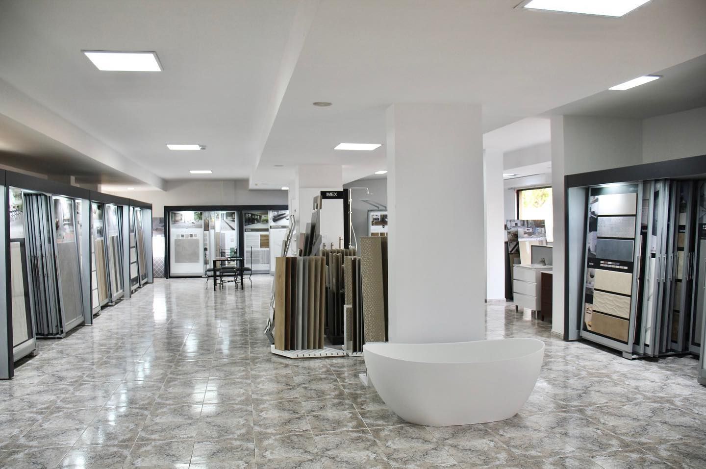 Interior luminoso de la sala de exposición con suelos de baldosas, estanterías de exhibición y una columna blanca en el centro.