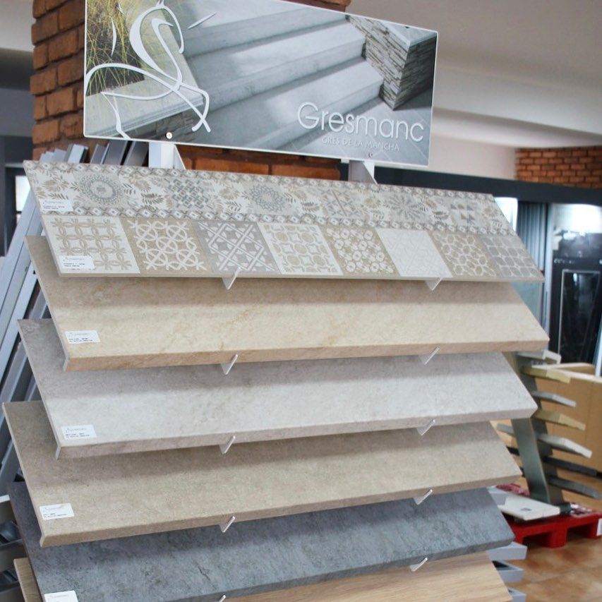 Estantería de exhibición de azulejos con múltiples paneles de muestras beige y gris en la sala de exposición de una tienda.