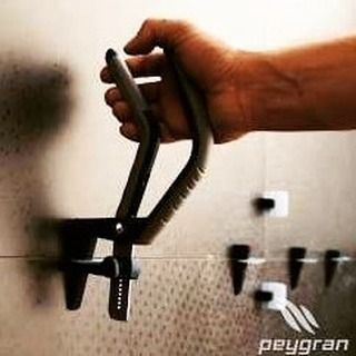 Mano que sostiene un mango negro con clip, sujeto a un dispositivo montado en la pared con pequeños ganchos.