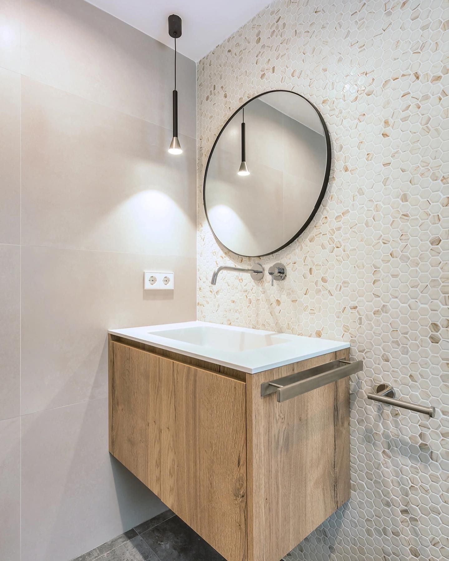 Tocador de baño moderno con espejo redondo, mueble de madera, lavabo blanco y apliques de pared.