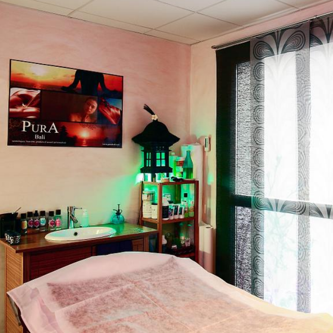 Salle de soins esthétique avec une table de massage, un meuble contenant des produits de bien‑être et une affiche décorative au mur.