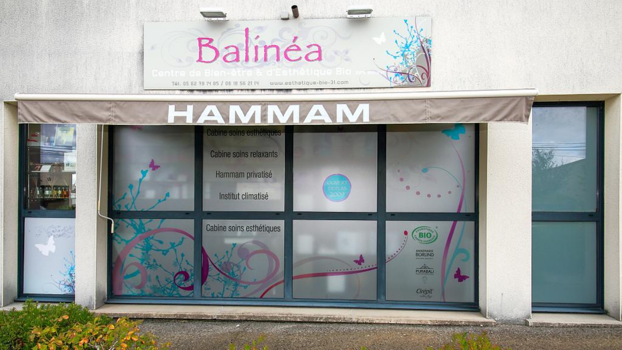 Façade du centre de bien‑être Balinéa avec un store affichant Hammam et des vitrages décorés de motifs floraux et papillons.