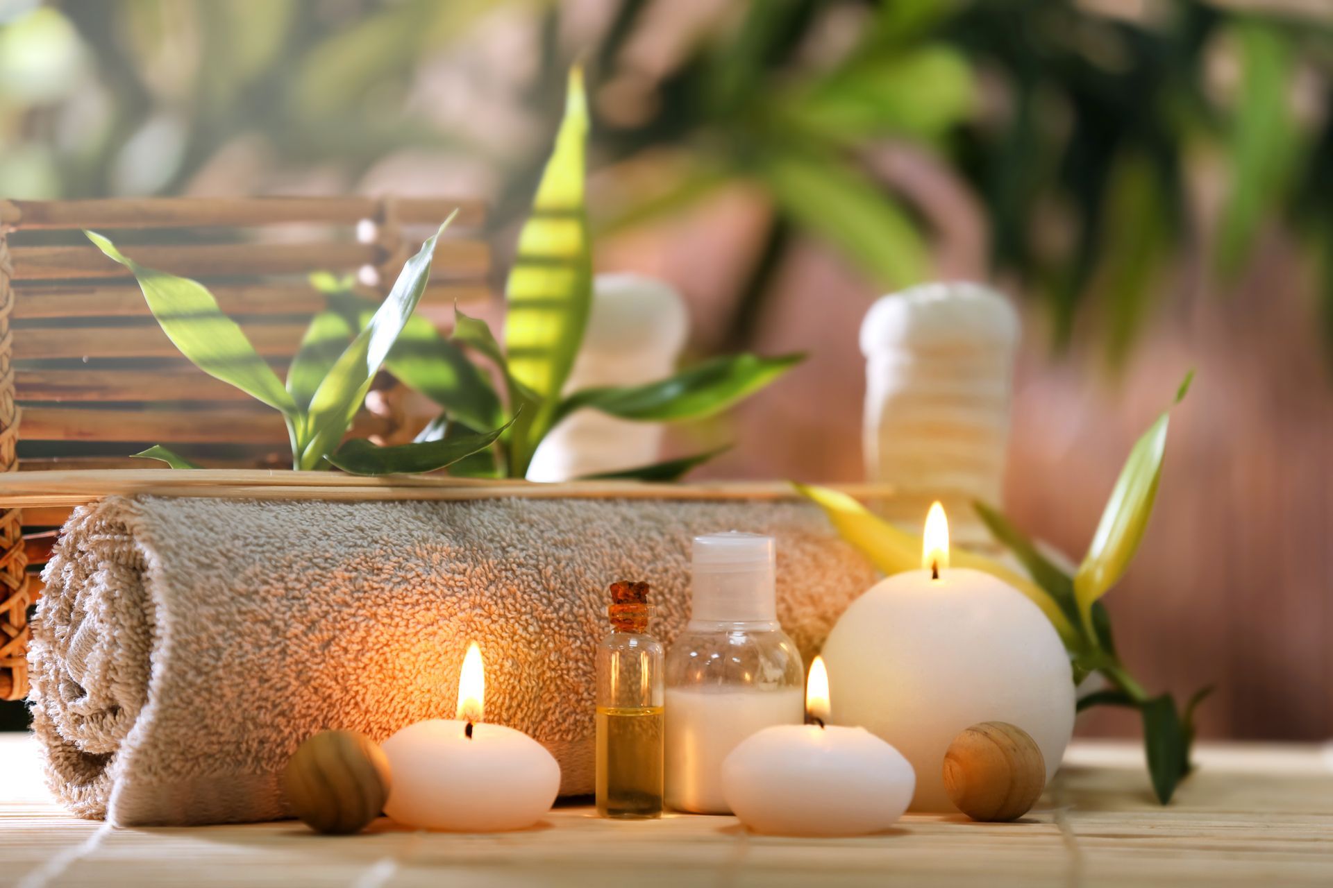 Spa avec bougies allumées, serviettes roulées et flacons d'huiles essentielles sur un plateau en bois avec des feuilles vertes