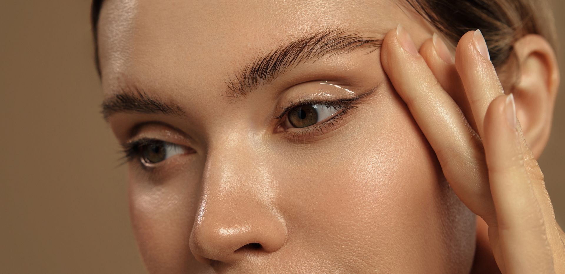 Une personne soulève délicatement la peau au-dessus de ses sourcils avec deux doigts, révélant des sourcils texturés et naturels ainsi qu'une peau éclatante.