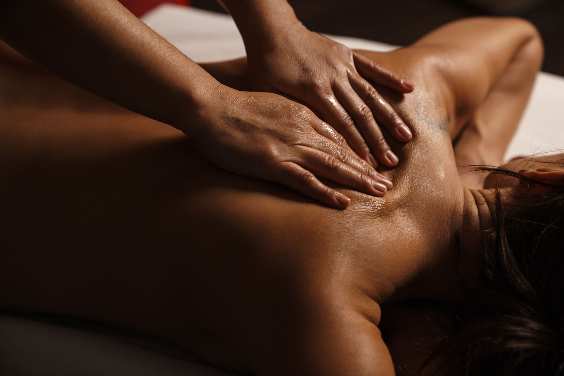 Des mains massent le dos d'une peau nue dans une lumière chaude et tamisée