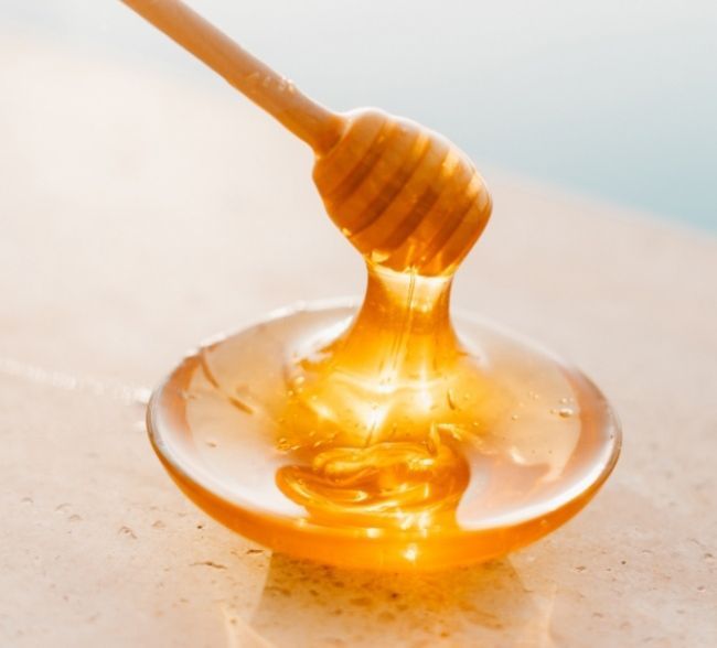Miel dans une coupelle accompagnée d'une cuillère à miel en bois