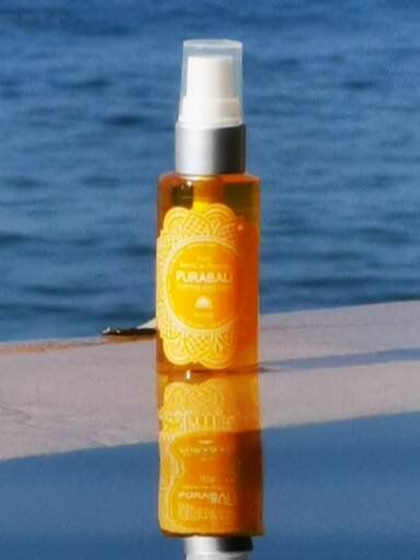 Flacon ambré d'huile Pura Bali à pompe blanche, se reflétant sur une surface se détachant sur une mer bleue floue