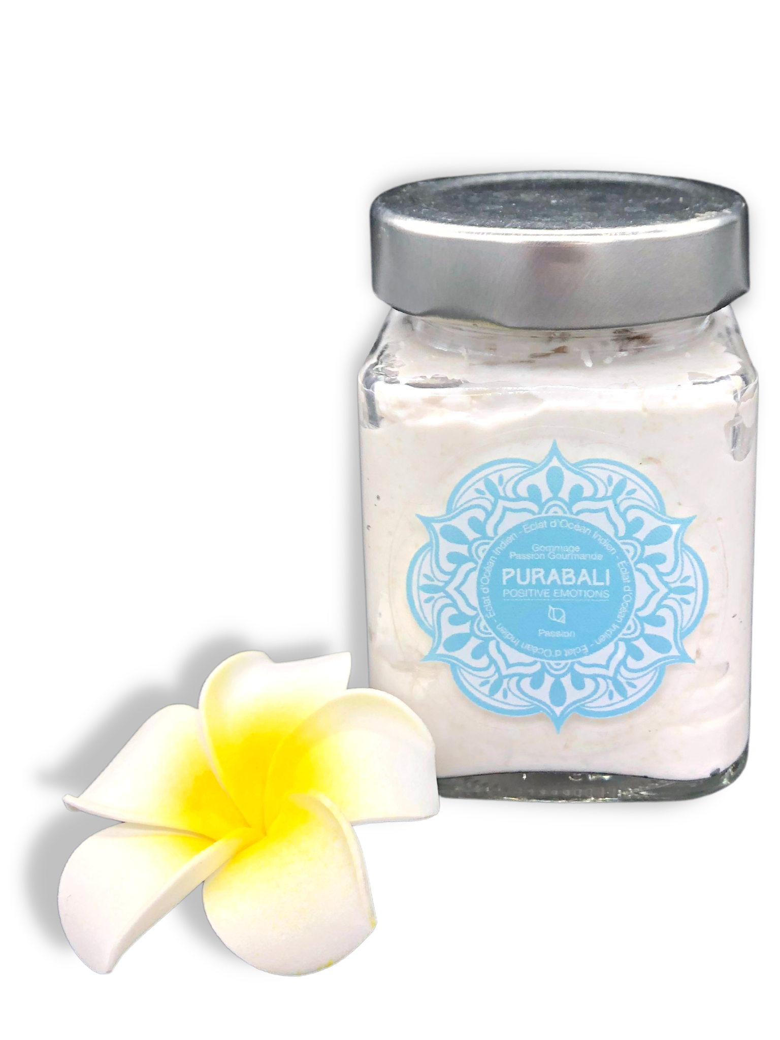 Pot de gommage avec une étiquette bleue, à côté d'une fleur de frangipanier blanche et jaune