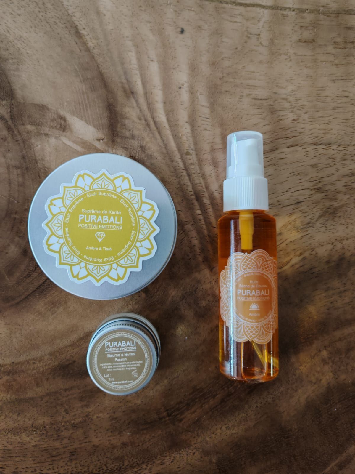 Flacon vaporisateur ambré, boîte ronde en métal et pot à couvercle jaune posés sur une surface en bois
