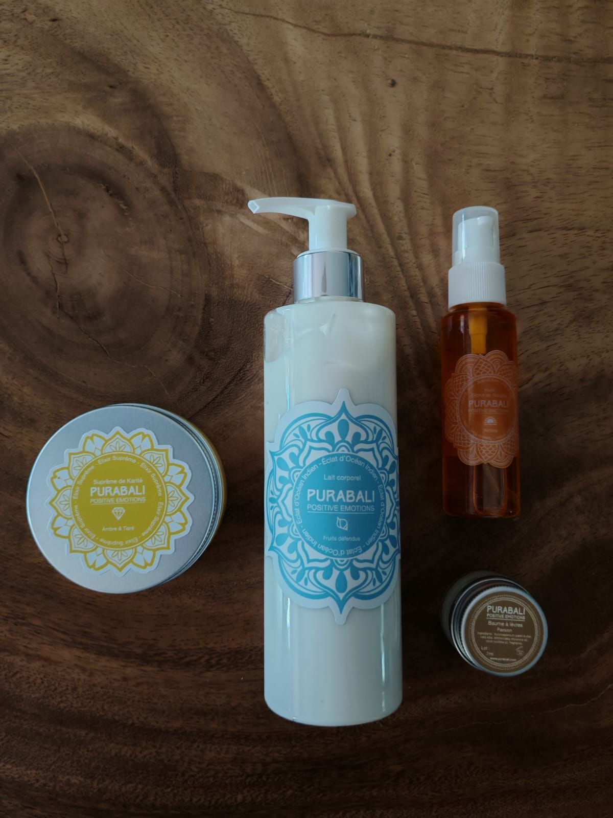 Quatre produits de soin pour la peau posés sur une surface en bois : un flacon pompe blanc, un flacon vaporisateur ambré et deux petits pots