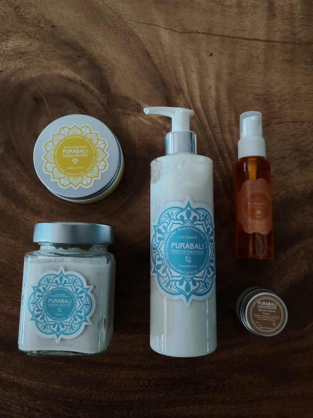 Cinq pots et flacons de soins pour la peau à étiquettes bleues, disposés sur une surface en bois