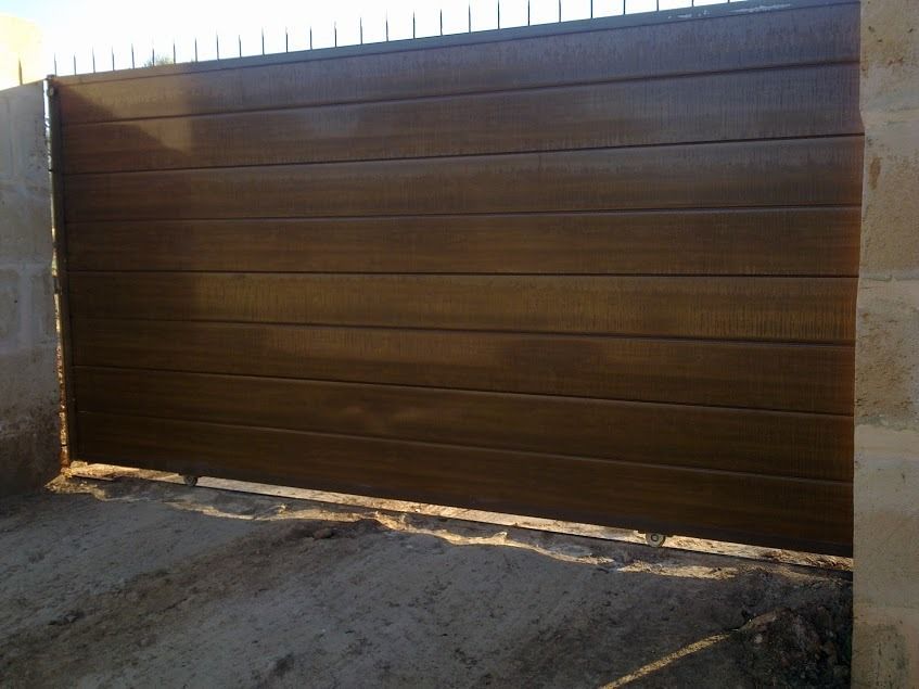 Una gran puerta de madera se encuentra en un camino de tierra al lado de un muro de piedra.