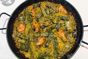 Sartén negra con curry de verduras naranjas y verdes sobre una superficie blanca.