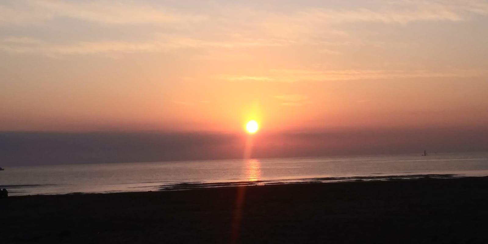 El sol se pone sobre un océano en calma, con la luz anaranjada reflejándose en el agua.