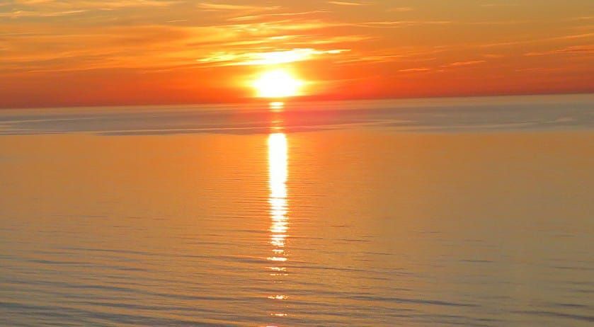 Puesta de sol anaranjada sobre aguas tranquilas con un brillante reflejo en el horizonte.