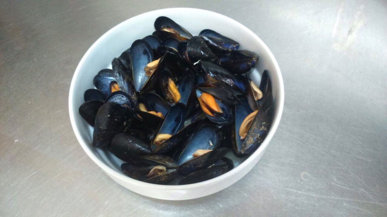 Un cuenco de mejillones cocidos sobre una superficie metálica.