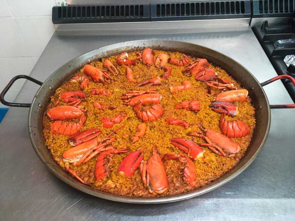 Gran paellera con arroz, gambas y langosta sobre la estufa.