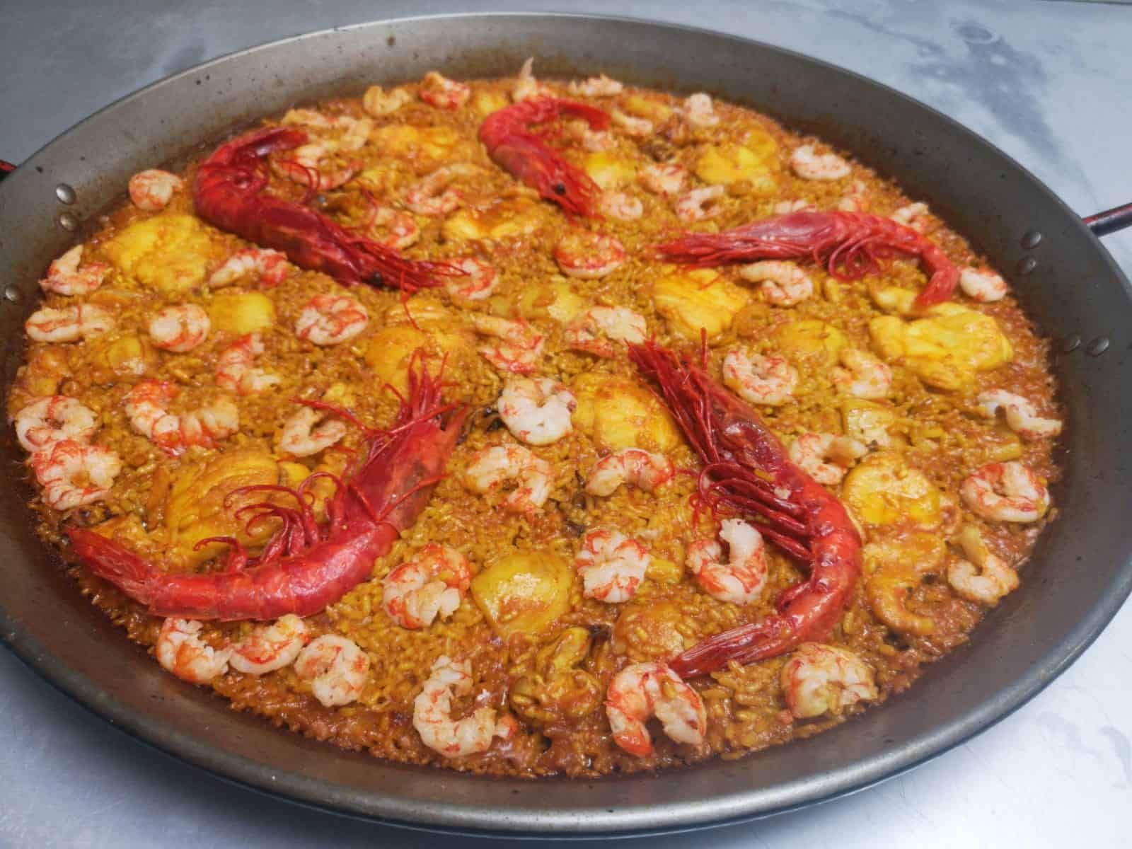 Paella en una paellera redonda, cubierta con gambas y pimientos rojos.