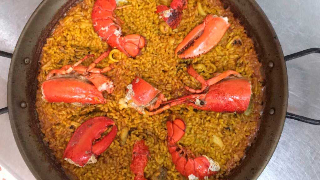 Sartén de arroz amarillo cubierta con trozos de langosta de color rojo brillante sobre una estufa.