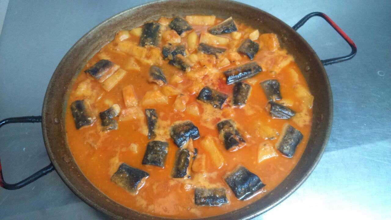 Sartén redonda de curry de naranja con trozos de verduras oscuras sobre una superficie azul.
