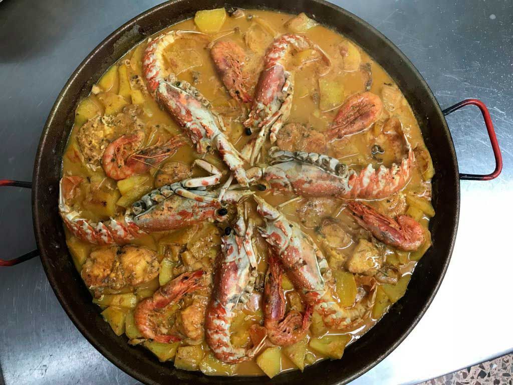 Paella de mariscos con arroz, camarones, mejillones y rodajas de limón en una sartén negra.