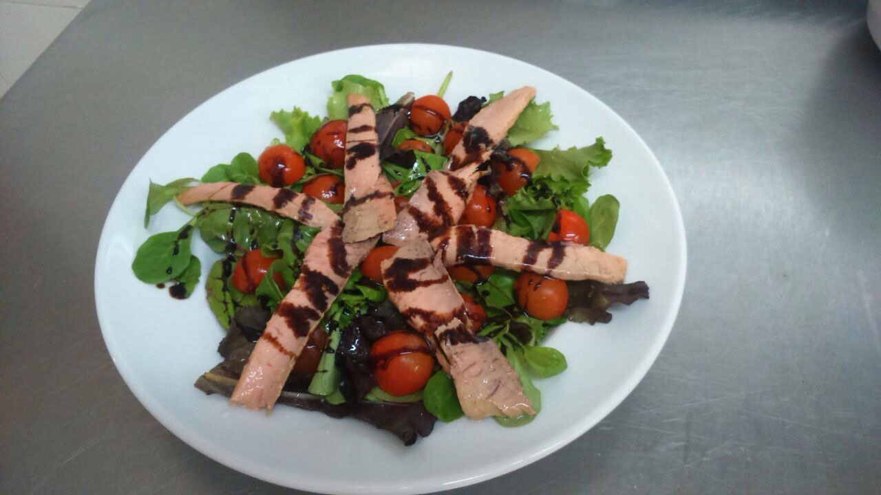 Ensalada de pollo a la parrilla con hojas verdes variadas, tomates cherry y un chorrito de vinagre balsámico en un plato blanco.