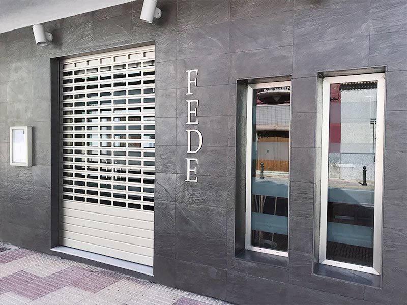 Fachada moderna con revestimiento negro, contraventana de seguridad blanca y letrero vertical 
